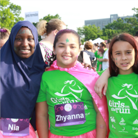 Two Girls on the Run participants smile at the camera while running at an outdoor practice in yellow shirts